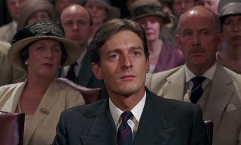 Movie still from “A Passage to India” (1984), directed by David Lean – A man in a suit and tie in front of a group of people; Close Up shot, Low angle