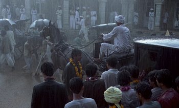 Movie still from “A Passage to India” (1984), directed by David Lean – A group of people gathered around a horse drawn carriage in the rain; Wide shot, High angle