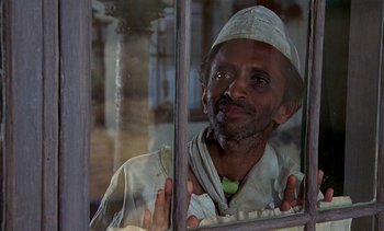 Movie still from “A Passage to India” (1984), directed by David Lean – A man looking out of a window at a building; Medium shot, Low angle