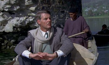 Movie still from “A Passage to India” (1984), directed by David Lean – A man sitting on the ground next to another man holding a stick; Medium shot, Over the shoulder angle