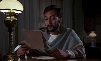 Movie still from “A Passage to India” (1984), directed by David Lean – A man sitting at a table looking at a piece of paper; Close Up shot, Low angle