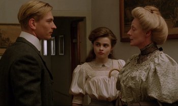 Movie still from “A Room with a View” (1985), directed by James Ivory – Two women and a man standing next to each other in a room; Medium shot, Over the shoulder angle