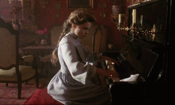 Movie still from “A Room with a View” (1985), directed by James Ivory – A young woman playing a piano in a living room; Medium shot, High angle