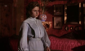 Movie still from “A Room with a View” (1985), directed by James Ivory – A woman in a dress standing in a room; Medium shot, Over the shoulder angle