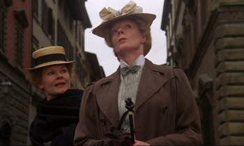 Movie still from “A Room with a View” (1985), directed by James Ivory – A woman wearing a hat and a coat on a city street; Close Up shot, Low angle