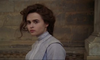 Movie still from “A Room with a View” (1985), directed by James Ivory – A young woman in a blue shirt is standing in front of a brick wall; Close Up shot, High angle