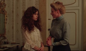 Movie still from “A Room with a View” (1985), directed by James Ivory – A woman talking to another woman in a room; Medium shot, Over the shoulder angle