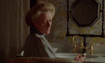 Movie still from “A Room with a View” (1985), directed by James Ivory – An older woman sitting at a bathroom sink; Medium shot, Over the shoulder angle