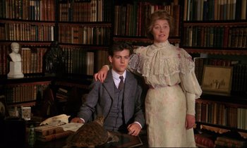 Movie still from “A Room with a View” (1985), directed by James Ivory – A man and a woman pose for a picture in front of a bookshelf; Medium shot, Low angle