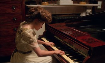 Movie still from “A Room with a View” (1985), directed by James Ivory – A woman in a white dress is playing a piano; Medium shot, High angle