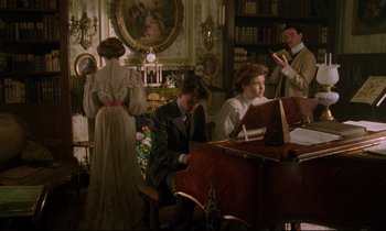Movie still from “A Room with a View” (1985), directed by James Ivory – A group of people sitting around a piano in a living room; Wide shot, High angle