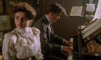 Movie still from “A Room with a View” (1985), directed by James Ivory – A man and a woman are playing the piano; Medium shot, Low angle