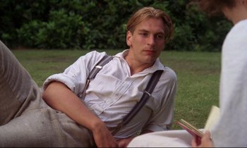 Movie still from “A Room with a View” (1985), directed by James Ivory – A man sitting on the grass with a book in his hand; Medium shot, Low angle