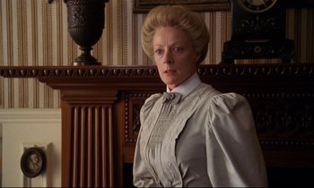 Movie still from “A Room with a View” (1985), directed by James Ivory – An older woman wearing a white dress standing next to a wall; Medium shot, Low angle