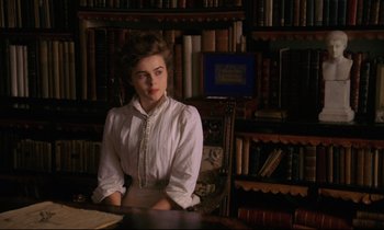 Movie still from “A Room with a View” (1985), directed by James Ivory – A woman sitting at a desk in a room full of bookshelves; Medium shot, High angle