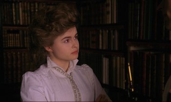 Movie still from “A Room with a View” (1985), directed by James Ivory – A woman in a white shirt is sitting in front of a book shelf; Close Up shot, Low angle