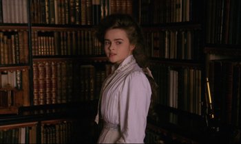 Movie still from “A Room with a View” (1985), directed by James Ivory – A young woman in a white dress standing in front of a book shelf; Medium shot, Low angle