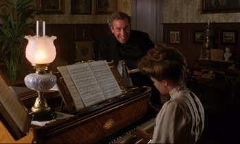Movie still from “A Room with a View” (1985), directed by James Ivory – A man sitting at a piano with a young boy; Medium shot, Over the shoulder angle