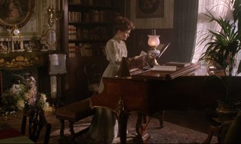 Movie still from “A Room with a View” (1985), directed by James Ivory – A woman standing at a desk in front of a piano; Wide shot, High angle