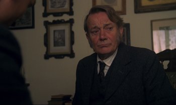 Movie still from “A Room with a View” (1985), directed by James Ivory – An older man wearing a suit and tie in front of a wall; Close Up shot, Over the shoulder angle
