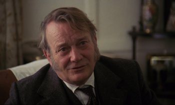 Movie still from “A Room with a View” (1985), directed by James Ivory – An older man wearing a suit and a tie; Close Up shot, Over the shoulder angle