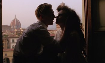 Movie still from “A Room with a View” (1985), directed by James Ivory – A man and a woman kissing in front of a city skyline; Medium shot, Low angle