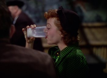 Movie still from “A Star Is Born” (1937), directed by Victor Fleming – A woman drinking a glass of water while wearing a hat; Medium shot, High angle