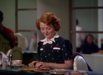 Movie still from “A Star Is Born” (1937), directed by Victor Fleming – A woman sitting at a table with a plate in front of her; Medium shot, Over the shoulder angle
