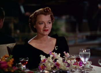 Movie still from “A Star Is Born” (1937), directed by Victor Fleming – A woman sitting at a dinner table with flowers in front of her; Medium shot, Over the shoulder angle