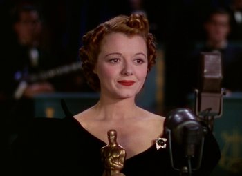 Movie still from “A Star Is Born” (1937), directed by Victor Fleming – A woman holding an award in front of a microphone; Close Up shot, Low angle