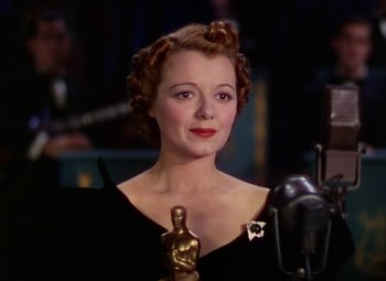 Movie still from “A Star Is Born” (1937), directed by Victor Fleming – A woman holding an award in front of a microphone; Close Up shot, Low angle