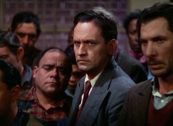 Movie still from “A Star Is Born” (1937), directed by Victor Fleming – A man in a suit and tie standing in front of a group of men; Medium shot, Low angle