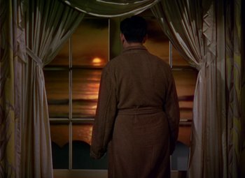 Movie still from “A Star Is Born” (1937), directed by Victor Fleming – A man standing in front of a window looking out at the sunset; Wide shot, Low angle