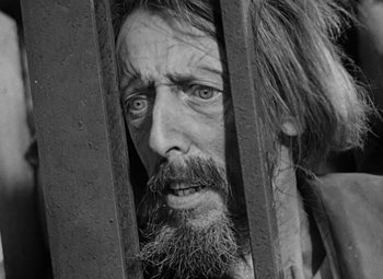 Movie still from “A Tale of Two Cities” (1935), directed by Jack Conway – A man with a beard and long hair looking through a fence; Close Up shot, Over the shoulder angle