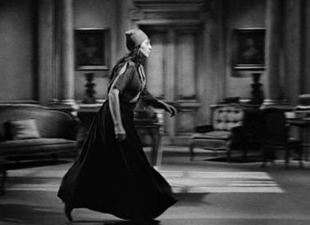 Movie still from “A Tale of Two Cities” (1935), directed by Jack Conway – A woman in a black dress is walking in a living room; Wide shot, High angle