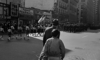 Movie still from “A Thousand Clowns” (1965), directed by Fred Coe – A black and white photo of a crowd of people marching down a street; Wide shot, High angle