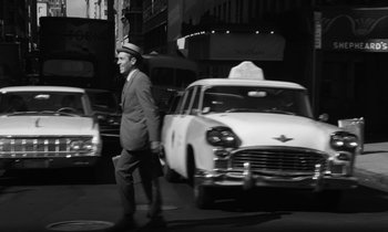 Movie still from “A Thousand Clowns” (1965), directed by Fred Coe – A man in a hat and a suit is crossing the street in front of a taxi cab; Wide shot, Low angle