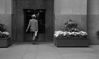 Movie still from “A Thousand Clowns” (1965), directed by Fred Coe – A man in a suit and a hat walking down a sidewalk; Wide shot, Over the shoulder angle