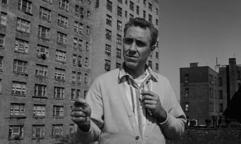 Movie still from “A Thousand Clowns” (1965), directed by Fred Coe – A black and white photo of a man holding a tie in front of a building; Medium shot, Low angle
