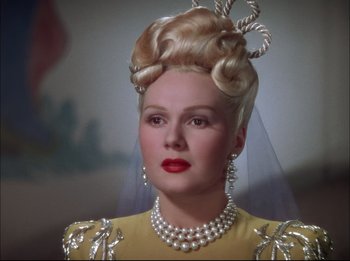 A woman in a yellow dress with a veil and pearls