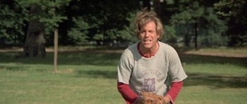 Movie still from “A Touch of Class” (1973), directed by Melvin Frank – A man holding a baseball glove on top of a grass covered field; Medium shot, Low angle