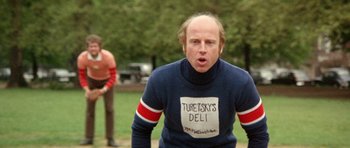 Movie still from “A Touch of Class” (1973), directed by Melvin Frank – A bald man in a blue sweater is standing in the grass; Medium shot, Low angle