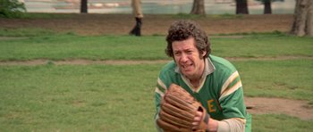 Movie still from “A Touch of Class” (1973), directed by Melvin Frank – A man holding a catchers mitt on top of a grass covered field; Medium shot, Low angle