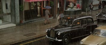 Movie still from “A Touch of Class” (1973), directed by Melvin Frank – A woman walking down the street with an umbrella over her head; Wide shot, High angle