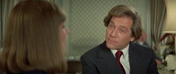 Movie still from “A Touch of Class” (1973), directed by Melvin Frank – A man in a business suit talking to a woman in a red tie; Close Up shot, Over the shoulder angle