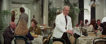 Movie still from “A Touch of Class” (1973), directed by Melvin Frank – An older man in a white jacket and a woman in a brown suit; Medium shot, Over the shoulder angle