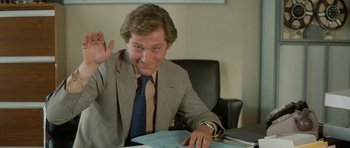 Movie still from “A Touch of Class” (1973), directed by Melvin Frank – A man sitting at a desk in front of papers; Medium shot, Low angle