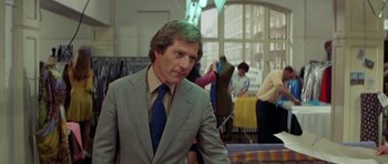 Movie still from “A Touch of Class” (1973), directed by Melvin Frank – A man in a suit and tie standing in front of a window; Medium shot, Over the shoulder angle