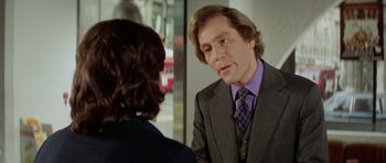 Movie still from “A Touch of Class” (1973), directed by Melvin Frank – A man wearing a suit and tie talking to another man; Medium shot, Over the shoulder angle