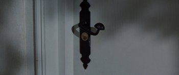 Movie still from “A Touch of Class” (1973), directed by Melvin Frank – A black door handle with a lock on a white wall; Extreme Close Up shot, High angle